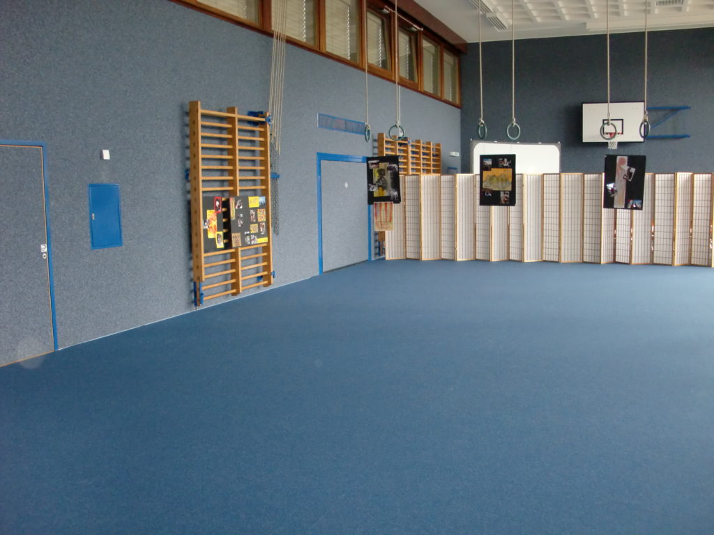 Salle de sport entièrement recouverte d'une protection de sol bleue pour une exposition, panneaux suspendus aux anneaux.