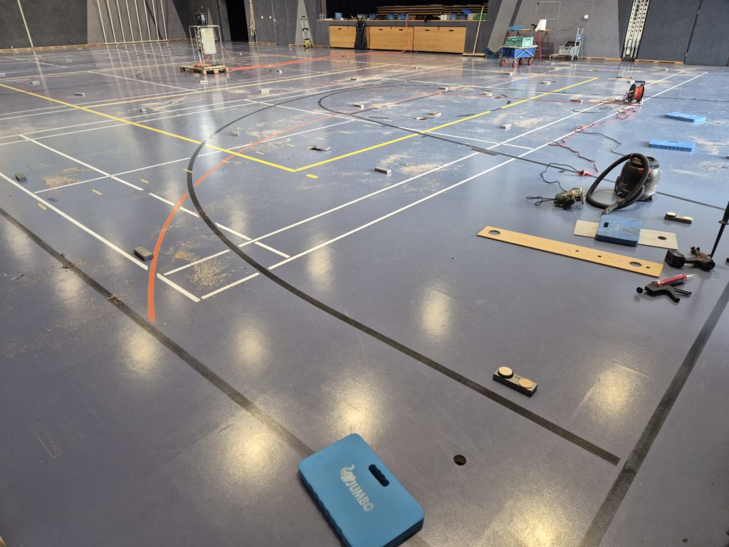 Rebouchage des percements d'assèchement dans un sol sportif : pièces collées et lestées, gabarit de perçage et outillage sur la surface