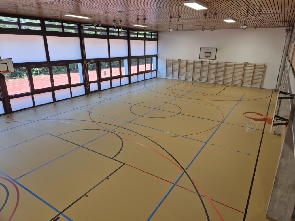 Salle de gymnastique scolaire après la rénovation de surface : sol en résine PU repeint et marquage refait aux normes.