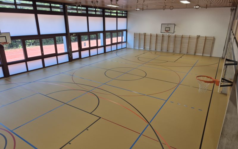 Salle de gymnastique scolaire après la rénovation de surface : sol en résine PU repeint et marquage refait aux normes.