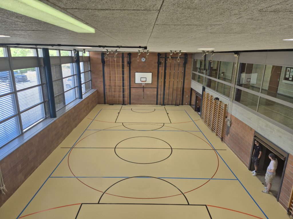 Vue d'ensemble d'une salle de gymnastique après le remplacement d'un ancien lino-liège par un sol sportif ProtecSport SP 40 avec marquage multisport