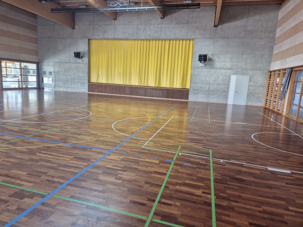 Salle polyvalente avec parquet sportif et scène, avant la pose de la protection de sol pour une manifestation