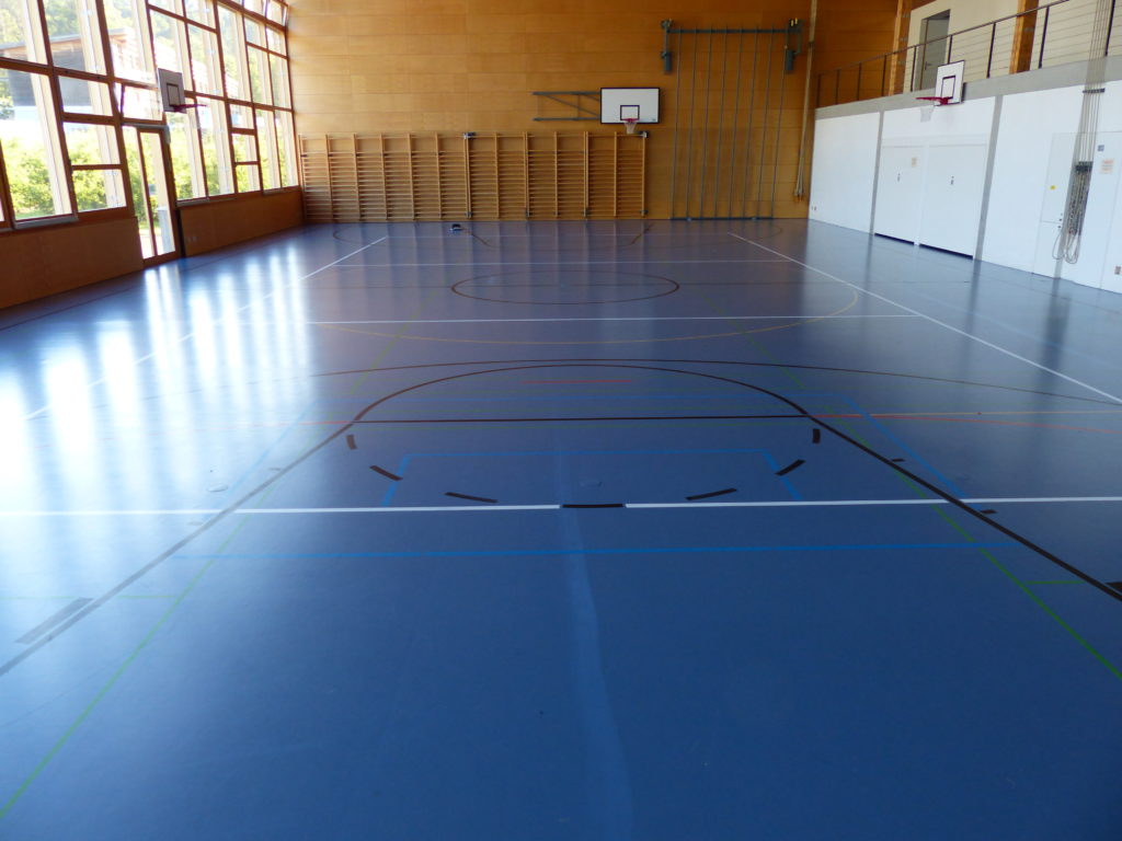 Sol sportif en résine bleu terni, avec une traînée blanche laissée par un produit de nettoyage inadapté