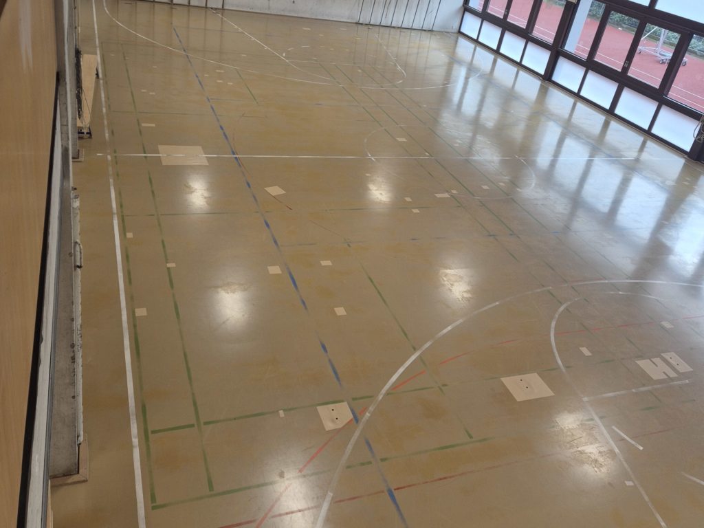 Sol sportif en résine PU avant rénovation : surface beige très usée et lignes de jeu presque effacées.