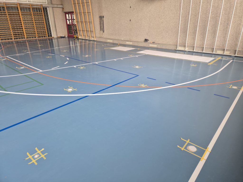 Sol sportif après assèchement : trous de percement rebouchés, encore entourés de scotch, et zone refaite le long du mur