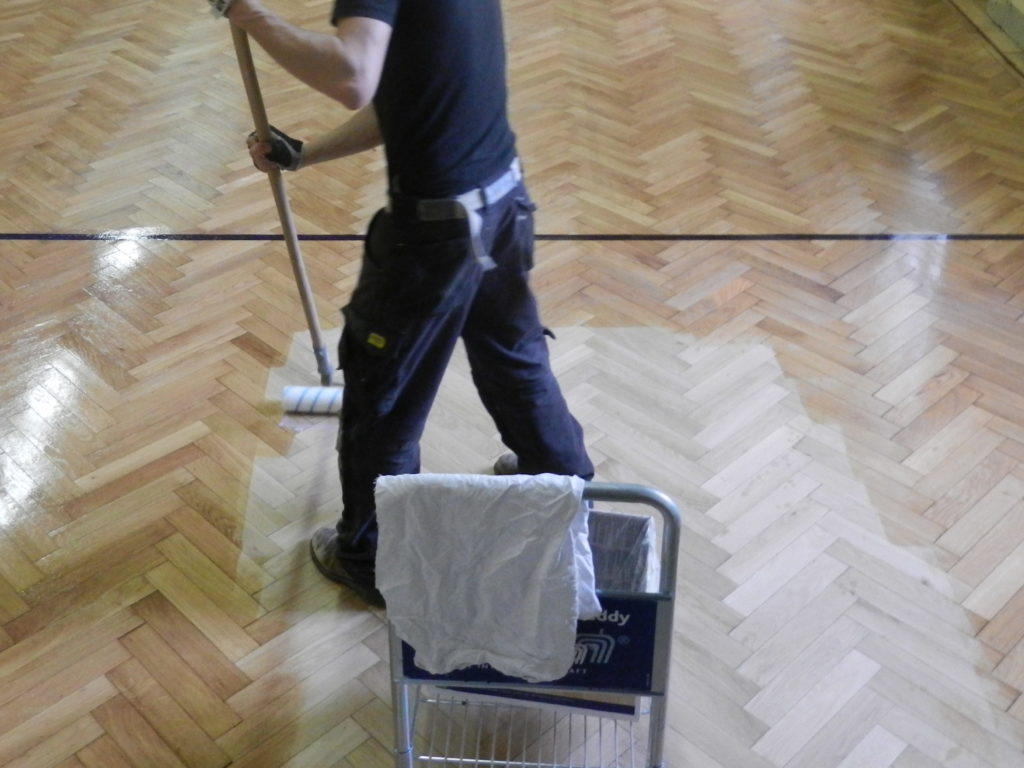 Application de la vitrification au rouleau sur le parquet en chêne poncé.